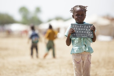 A girl holds a slate with the alphabet. Credit: UNICEF/UNI145619/Asselin A girl holds a slate with the alphabet. Credit: UNICEF/UNI145619/Asselin